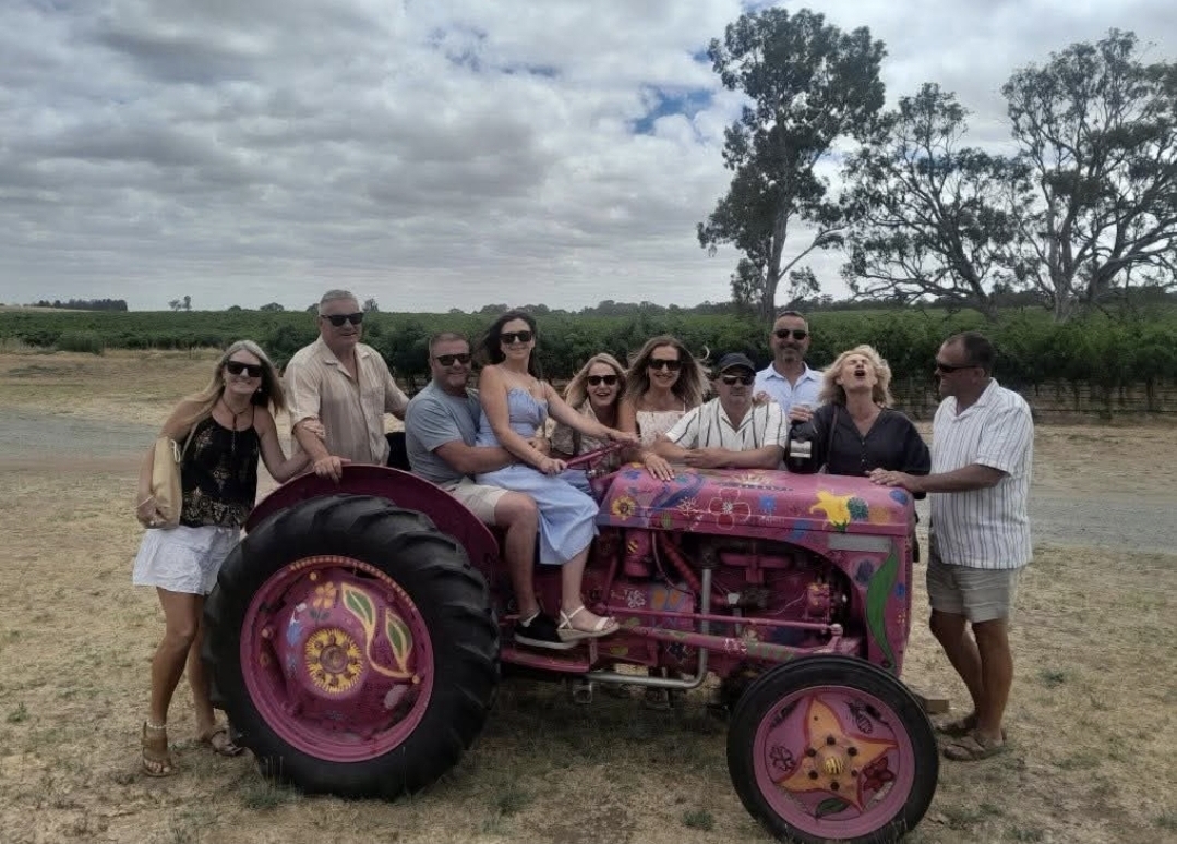 Happy tour group gathered around a colourful painted tractor in the vineyard